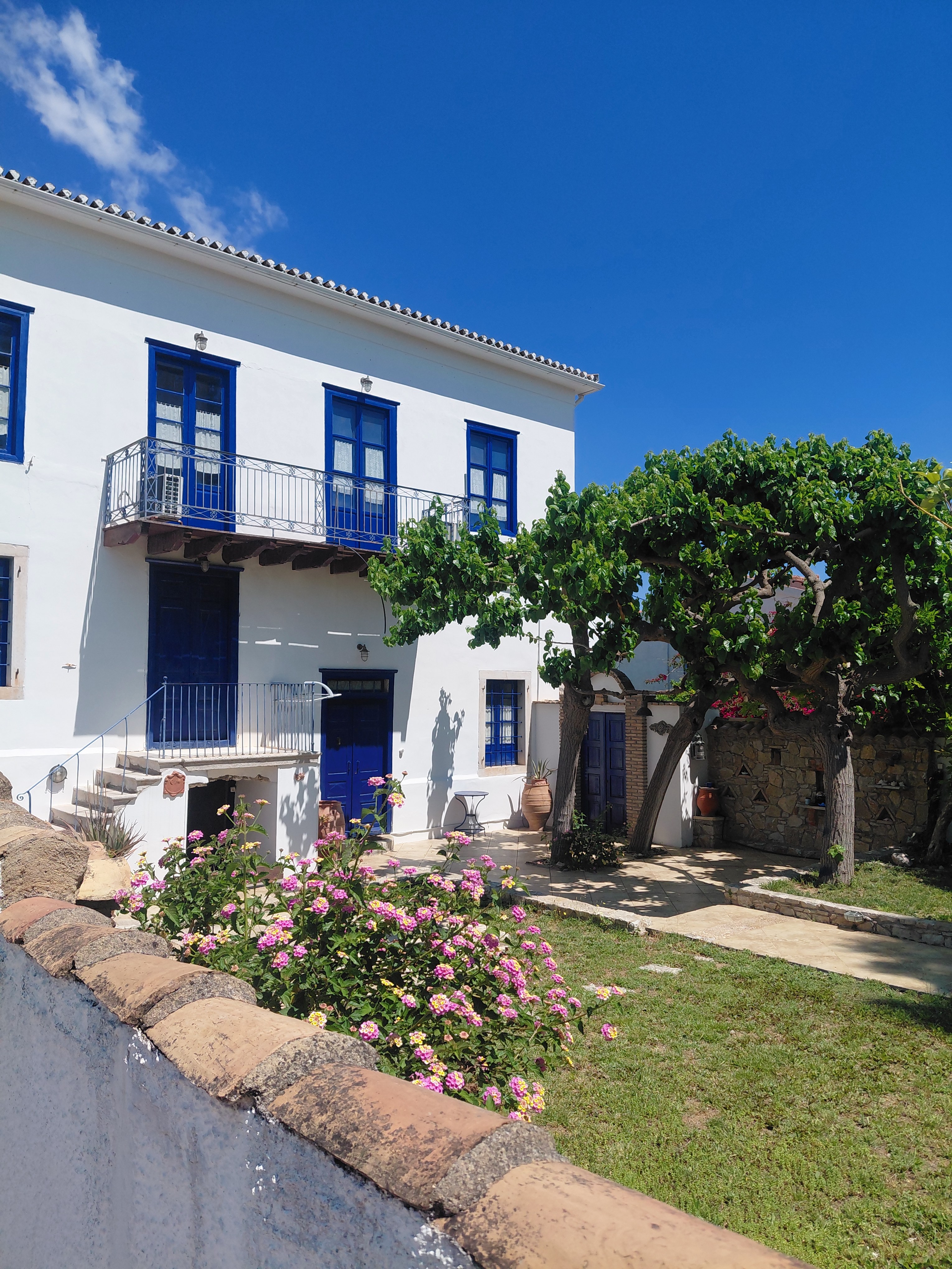 The garden elevation of the mansion — white walls, blue shutters, vine pergola and walled lawn
